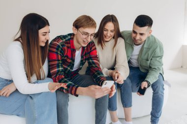 Bir grup mutlu genç arkadaş içeride kanepede otururken telefonda video izliyorlar.