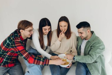 Bir grup mutlu arkadaş cips yiyor, sosyalleşiyor ve evde birlikte eğleniyorlar.