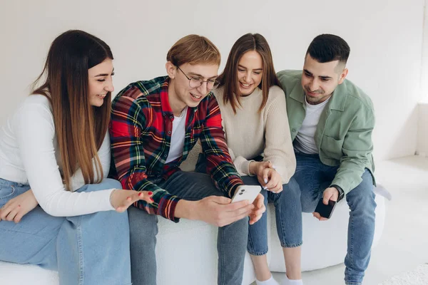 Bir grup mutlu genç arkadaş içeride kanepede otururken telefonda video izliyorlar.