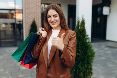 Young costumer woman hold package bags with purchases after shopping show thumb up