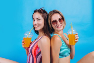 Plajda, güneş gözlüğü takan iki mutlu kızın portresi. Ellerinde turuncu kokteyller tutuyorlardı. Gülümsüyor ve yaz tatilinin tadını çıkarıyor. Yaz Sahil Denizi.