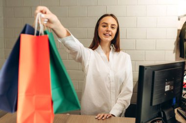 Giyim mağazasında satıcı müşteriye çanta veriyor.