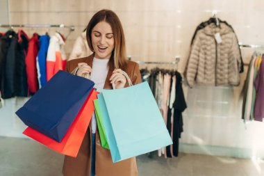 Giyim mağazasında alışveriş torbaları tutan mutlu genç bir kadın. Alışveriş konsepti. Satılık.