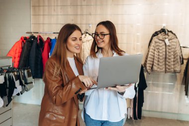 The seller uses a laptop to consult on clothing trends. The seller advises the girl