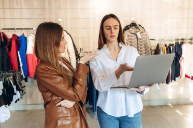The seller uses a laptop to consult on clothing trends. The seller advises the girl