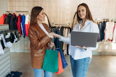The seller uses a laptop to consult on clothing trends. The seller advises the girl