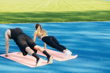 Arka taraftaki genç çift stadyumda şınav çekiyor.