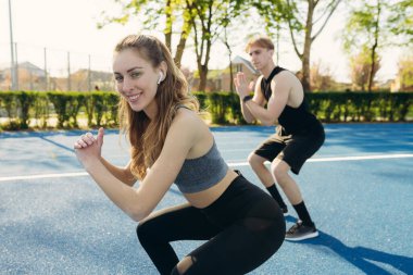 Mükemmel çömelme. Genç ve güzel bir çift stadyumda spor kıyafetleriyle antrenman yapıyor.