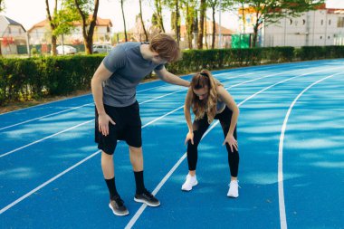 Gülümseyen zinde genç bir adam kız arkadaşını destekliyor. Sabahları dışarıda koştuktan sonra bitkin düşüyor.