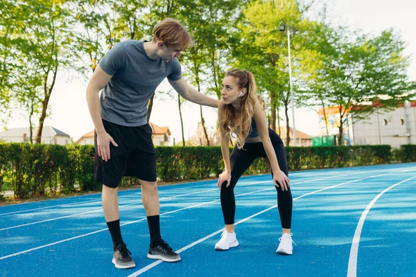 Gülümseyen zinde genç bir adam kız arkadaşını destekliyor. Sabahları dışarıda koştuktan sonra bitkin düşüyor.