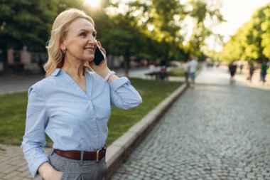 Yetişkin bir iş kadını cep telefonuyla konuşuyor, hoş bir sohbetin tadını çıkarıyor, mavi bir gömlek giyiyor. İş Başarı kavramı