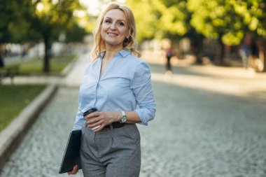 Portrait of successful mature businesswoman holding laptop and paper cup with coffee. Women of the 50s. The concept of work. Freelance. Success