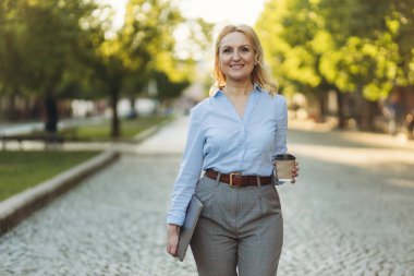 successful mature businesswoman holding laptop and paper cup with coffee. A woman in her 50s. The concept of work. Freelance. Success