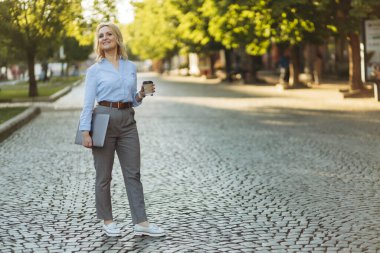 successful mature businesswoman holding laptop and paper cup with coffee. A woman in her 50s. The concept of work. Freelance. Success