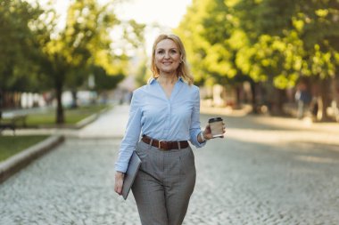 successful mature businesswoman holding laptop and paper cup with coffee. A woman in her 50s. The concept of work. Freelance. Success