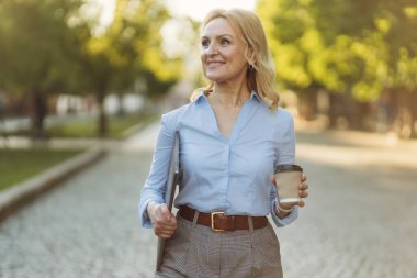 Portrait of a successful mature businesswoman wearing stylish clothes. Woman in her 50s. Woman holding laptop and paper cup of coffee. Lifestyle and work concept