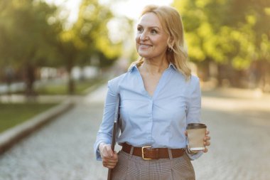 Portrait of a successful mature businesswoman wearing stylish clothes. Woman in her 50s. Woman holding laptop and paper cup of coffee. Lifestyle and work concept