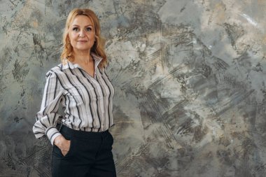 Çekici, kendinden emin Avrupalı olgun bir kadının desenli mermer duvara karşı poz verdiği, gömlek ve pantolon giydiği, başarılı bir iş kadını.