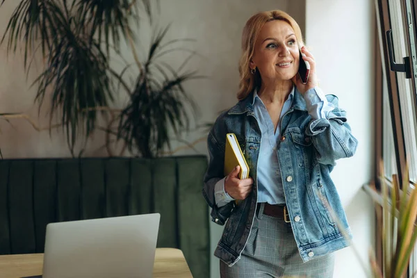 Kafede dikilip telefonla konuşan olgun bir kadının portresi.