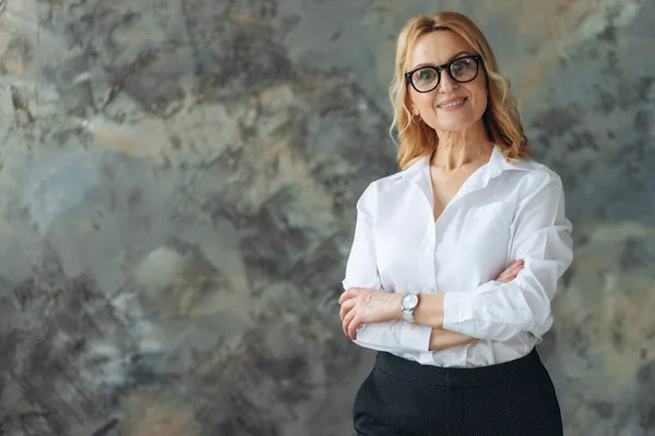 Orta yaşlı sarışın iş kadını gözlüklü, izole edilmiş arka planda duran mutlu yüzlü, kollarını kavuşturup kameraya bakan. Pozitif kişi. Metin için yer