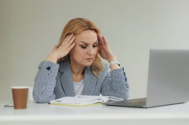 Yorgun yaşlı iş kadını içeride çalışmak için dizüstü bilgisayar kullanıyor. Güzel, yaşlı bir bayanın çok çalıştığı için başı ağrıyor. Olgun kadın 50 'li yaşlarda. Yakın plan iş kadını portresi
