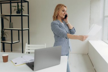 50 yaşında ciddi bir iş kadını akıllı telefondan konuşuyor, evrak okuyor, kurumsal iş sorununu çözüyor. Kadın çalışan cep telefonuyla belgeyi tartışıyor, haberleri alıyor