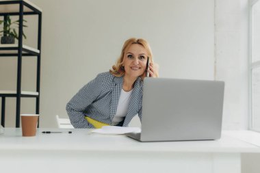 Takım elbiseli orta yaşlı takım lideri cepte duruyor ve elinde bir defter var. Olgun bir kadın cep telefonuyla konuşuyor.