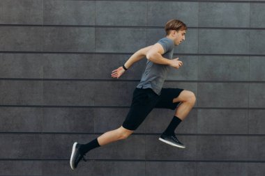 Siyah duvarın yanında koşan ve zıplayan genç sporcunun tüm vücudu.