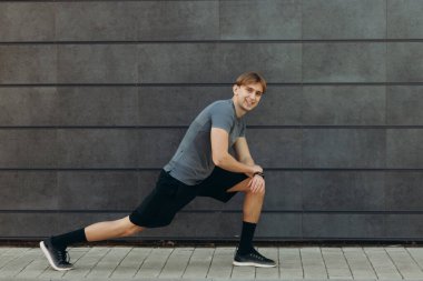 Genç adam siyah duvara karşı esneme hareketleri yapıyor.