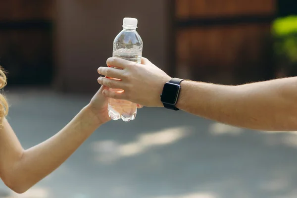 Young girl gives a plastic bottle of clean water to her husband. close up of hands.