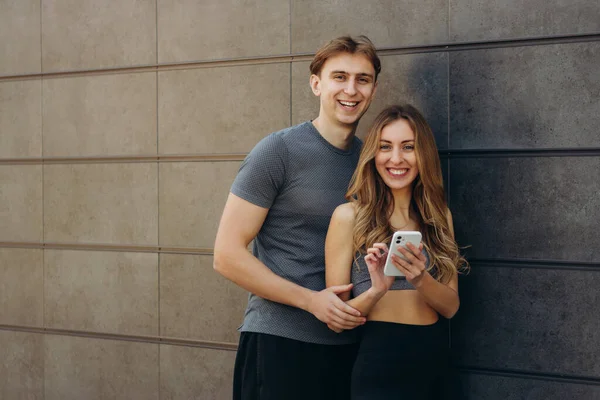 Sorrindo Casal Desportivo Usando Telefone Celular Parede Cinza — Fotografia de Stock