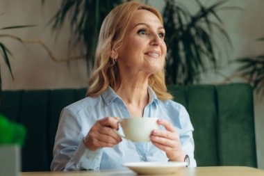 Bir fincan kahveyle orta yaşlı güzel bir kadının yakın plan portresi. Olgun kadın 50 'li yaşlarda.