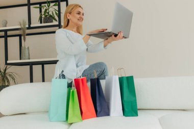 Yetişkin bir kadın evde bilgisayarla alışveriş yapıyor. İnternetten sipariş veriyor. Alışveriş torbalarıyla çekici bir kadın. Çevrimiçi alışveriş kavramı