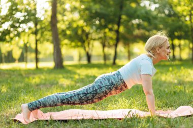 Yaşlı kadının yoga mat'ın bahçesinde tahta yapması