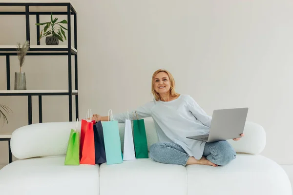 Mature woman shopping online at home on laptop. Woman makes an order online. Attractive woman with shopping bags. Online shopping concept