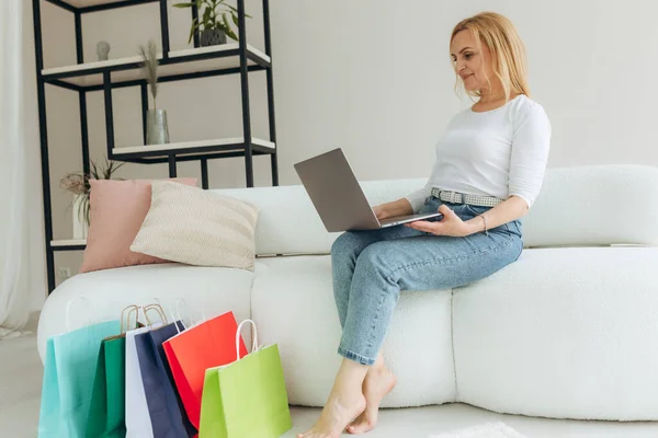 Mature woman shopping online at home on laptop. Woman makes an order online. Attractive woman with shopping bags. Online shopping concept