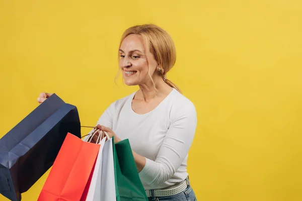 Reife Frau Auf Gelbem Hintergrund Erwägt Ihre Einkäufe — Stockfoto