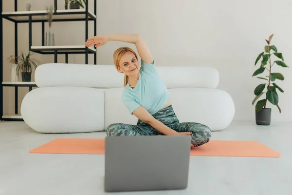 成熟时代的体育运动 快乐的老年女性在家里的笔记本电脑前做伸展运动 观看在线辅导 复制空间 — 图库照片