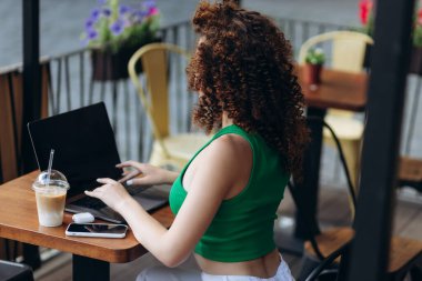 Kafede dizüstü bilgisayar kullanan kıvırcık bir kızın arka görüntüsü. Öğrenci