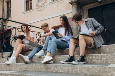 Confident students. Group of happy young people working together and looking at laptop while sitting on steps