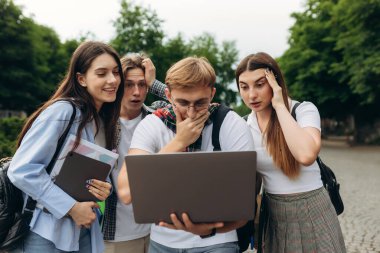It is incredibly! Surprised group of students looking at laptop and keeping mouth open while standing in park