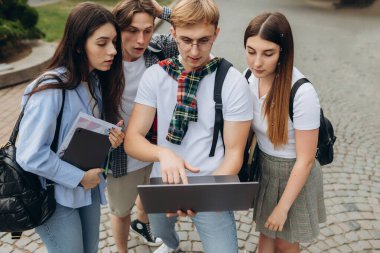 Four amazed friends are watching media content online on a laptop while standing on the street