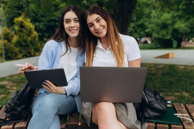 Beautiful two young girls work and study using gadgets. Students use laptop and tablet