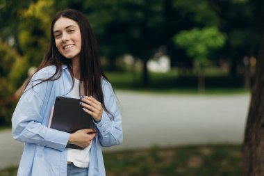 Young happy smiling caucasian young girl business student walking concept in the summer green park outdoor holding tablet. Copy space