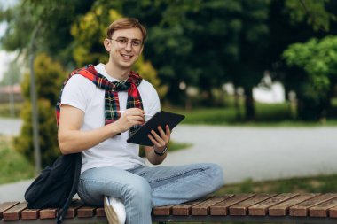 Happy smiling student outdoors with tablet. Emotion of joy. The concept of college education