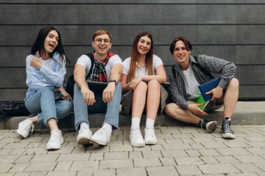 Group of happy smiling students sitting on the floor against dark wall. College learning concept