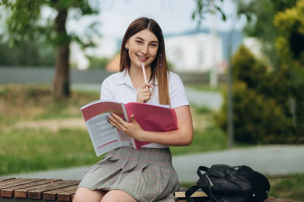 female college student thinking outside with bag and book