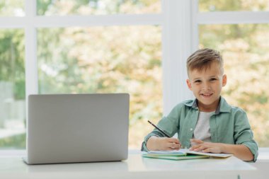 Schoolboy works with laptop while doing homework at home. Place for your text