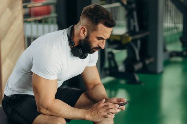 Spor salonunda egzersiz yaparken telefonu kullanan yakışıklı adam.