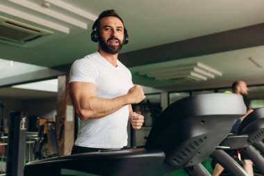 Side view of a handsome athlete running on a treadmill in the gym. The guy is wearing a white shirt